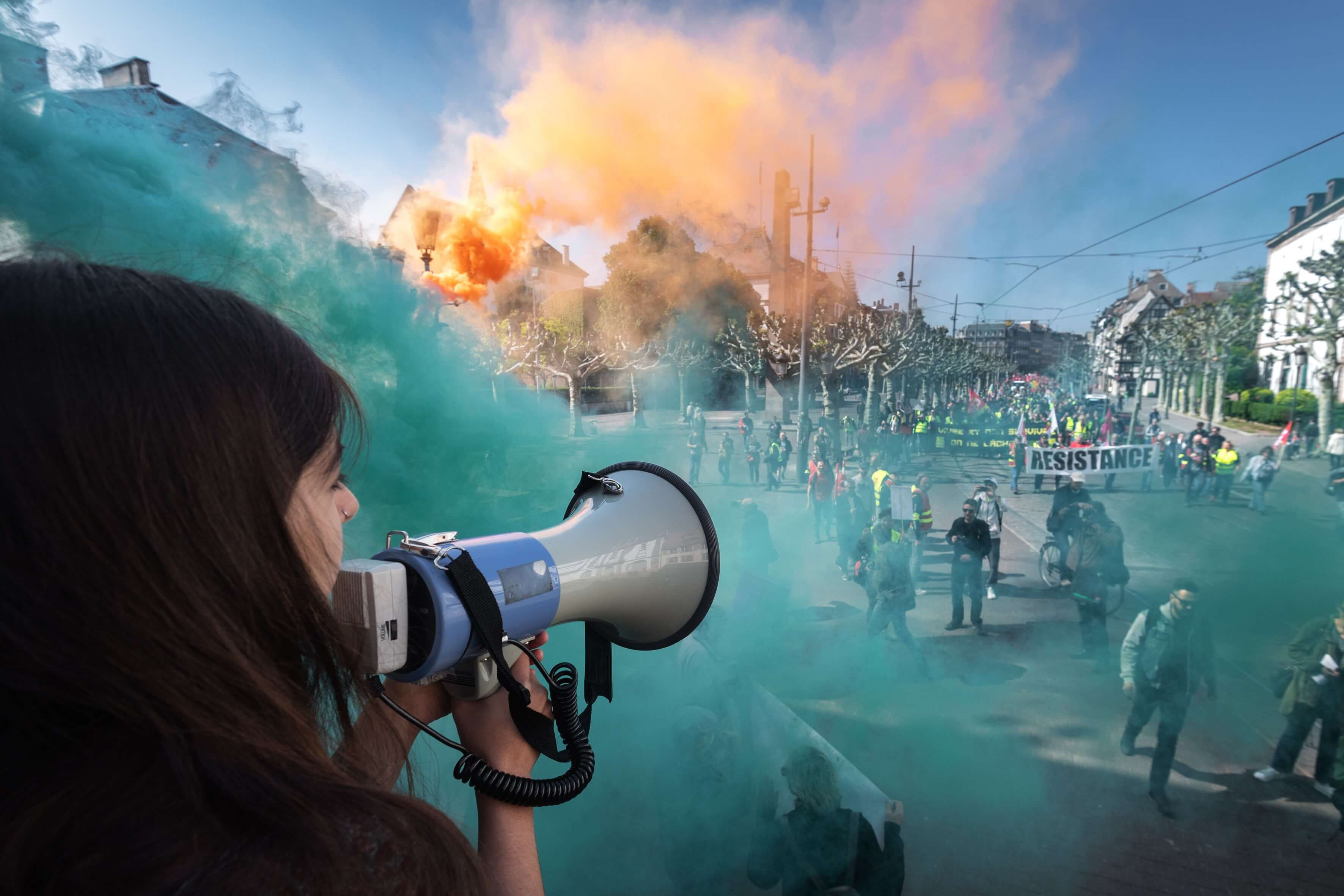 Un manifestant parle à travers un mégaphone alors que la fumée de bombes fumigènes colorées s'élève près des personnes participant au rassemblement annuel du 1er mai à Strasbourg, dans l'est de la France, le 1er mai 2019.